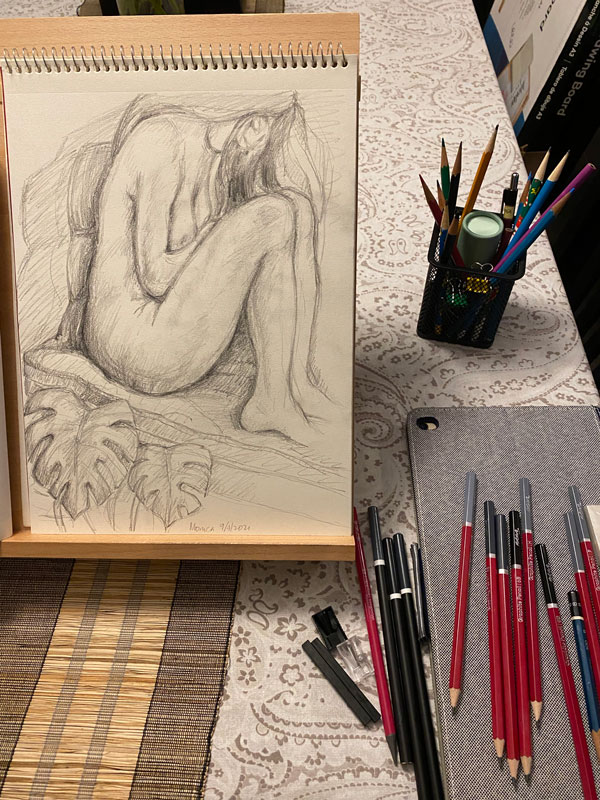 Sketch of nude woman curled up on couch on sketchpad, pencils